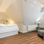 Schlafzimmer mit Dachschrägen, weißem Bett und grauem Sessel.