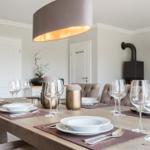 Esstisch mit Platz für sechs Personen, moderne Beleuchtung und Kamin im Hintergrund.