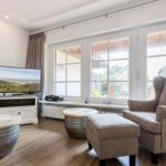 Ein Wohnzimmer mit Fernseher, Sessel und Fenstern zum Blick ins Freie.