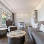 Wohnzimmer mit Sofa, Sitzgruppe und Essbereich. Fenster mit Blick auf Garten.