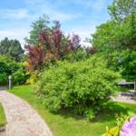 Garden with stone path, flowerbeds, and beach chair. House with thatched roof.
