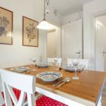 Dining room with wooden table, white chairs, and paintings on the wall.