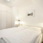 Bedroom with white bed, nightstands, and wardrobe.