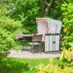 Garden with beach chair, table and chairs surrounded by green bushes.