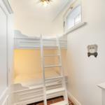 A bedroom with a bunk bed, white walls, and a small window.