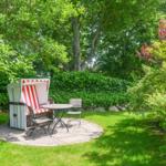 Circular stone patio with beach chair, table, and chairs in the green garden.