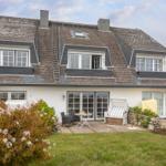 Haus mit Dachgauben, Terrasse und Garten. Weiße Fassade, Holzterrasse mit Möbeln.