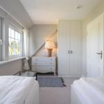 Zimmer mit zwei Betten, Schrank, Nachttisch und Fenstern.