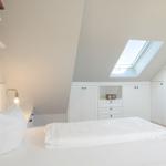 Schlafzimmer mit Dachfenster, weißem Bett und Schränken.