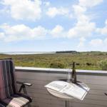 Terrasse mit Stuhl und Tisch. Blick auf Feld und Wasser unter blauem Himmel.