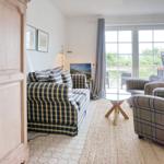 Living room with sofa, armchairs, and glass table. View to terrace with garden.