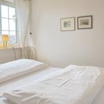 A bedroom with a white bed, window, and two pictures on the wall.