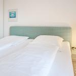 Double bed with white bedding and checkered headboard. Nightstand with lamp and wall art.