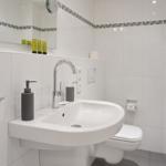 Bathroom with sink, mirror, and toilet. White tiles and gray accessories.
