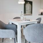 Dining room with white table and gray chairs, kitchen area in background.