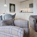 Two comfortable armchairs with checkered fabric, dining area and kitchen in background.