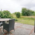 Terrace with table and chairs, surrounded by green areas and shrubs.
