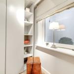 A room with a white wardrobe, a window, and a brown stool.