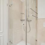 Shower with glass enclosure, showerhead, and handheld shower. White tiles and cabinet.