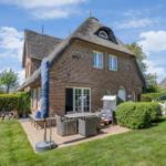 Red brick house with thatched roof and garden area with seating.