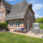 House with thatched roof, terrace with garden furniture and green lawn.