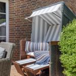 Terrace with beach chair, seating area, and green hedge in front of brick house