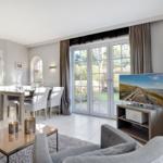 Living and dining area with TV, table, chairs, and windows to the garden.