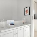 White cabinet with glass vases and picture on the wall. Kitchen in the background.