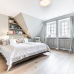 Schlafzimmer mit Dachschrägen, Bücherregal, Fenstern und Holzboden.