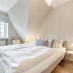 Schlafzimmer mit Dachschräge, Bett, Fenster und Nachttisch.