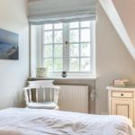 Schlafzimmer mit Dachschräge, Fenster, Stuhl und Nachttisch.