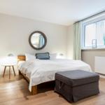 Schlafzimmer mit Bett, Nachttisch, Spiegel und Fenster.