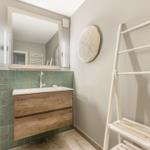 Badezimmer mit Waschbecken, Spiegel und Holzunterschrank. An der Wand hängt ein weißer Trockner.