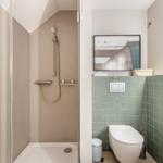 Dusche mit Duschbrause, Toilette und grüne Fliesenwand.