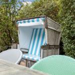 Strandkorb mit blau-weißem Stoff und geflochtenem Rahmen im Garten.