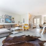 Wohn- und Essbereich mit Sofa, Tisch und Stühlen. Holzfußboden und Wandbildergalerie.