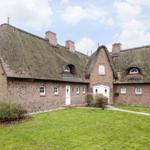 House with thatched roof and brown brick walls. Lawns and white doors.