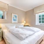 Bedroom with bed, two nightstands, and windows overlooking greenery.