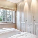 Bedroom with white bed, window, and white wardrobe doors.