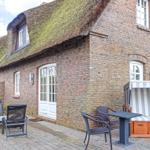 House with thatched roof and stone wall, outdoor area with table, chairs, and beach chair.