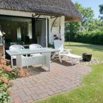Terrace with white garden furniture and lawn in front of a house with thatched roof.