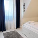 Bedroom with white bed, blue and white curtains, and gray rug.