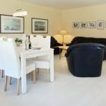 Dining area with white table and chairs. Living area with black leather chairs and wall pictures.