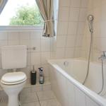 Bathroom with bathtub, toilet, and window with curtains.