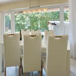 Dining room with white table and chairs, large window overlooking garden.