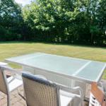 Terrace with table and chairs, view of green lawn and trees.