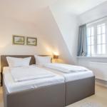 Schlafzimmer mit Doppelbett, Fenstern und Wandbildern.