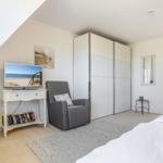 Schlafzimmer mit Bett, Kleiderschrank, Sessel und Fernseher.