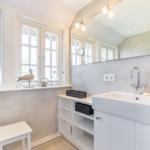Badezimmer mit Waschbecken, Spiegel und Fenstern.