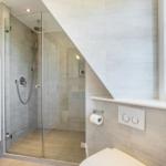 Dusche mit Glaswand, Toilette und Fenster im Badezimmer.